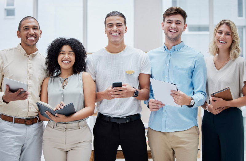 A group of five people at work standing and laughing into the camera